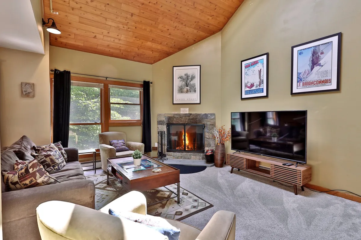 The image showcases a warm and inviting living area inside the Trail Creek condo. A cozy fireplace serves as the room’s focal point, flanked by plush sofas perfect for lounging. Large windows fill the space with natural light and offer peeks of the snowy Vermont landscape. The room is ideal for relaxing after a day on the slopes, gathering with friends or family, and enjoying leisure activities like movie nights or board games.