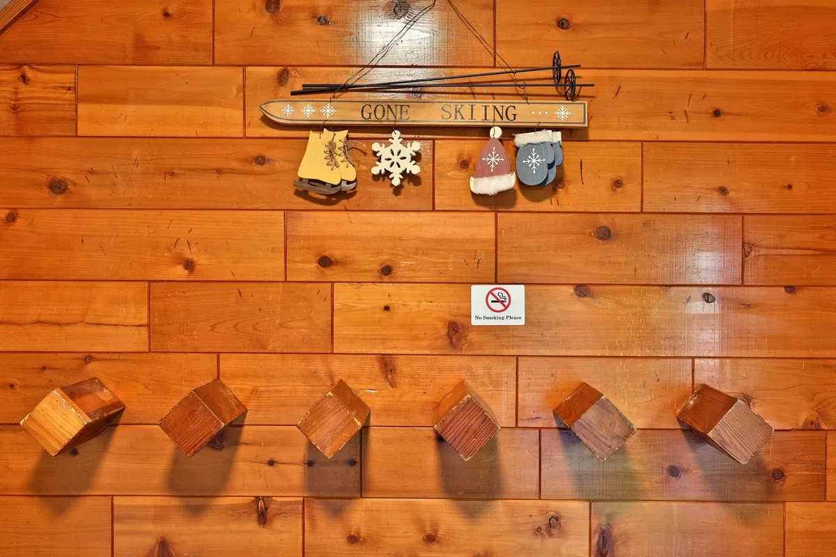 A playful mudroom or entrance area featuring a rustic 'GONE SKIING' sign, decorative ski equipment, hanging mittens, snowflakes, and wooden hooks. The scene evokes memories of winter sports and fun, celebrating the spirit of mountain recreation.