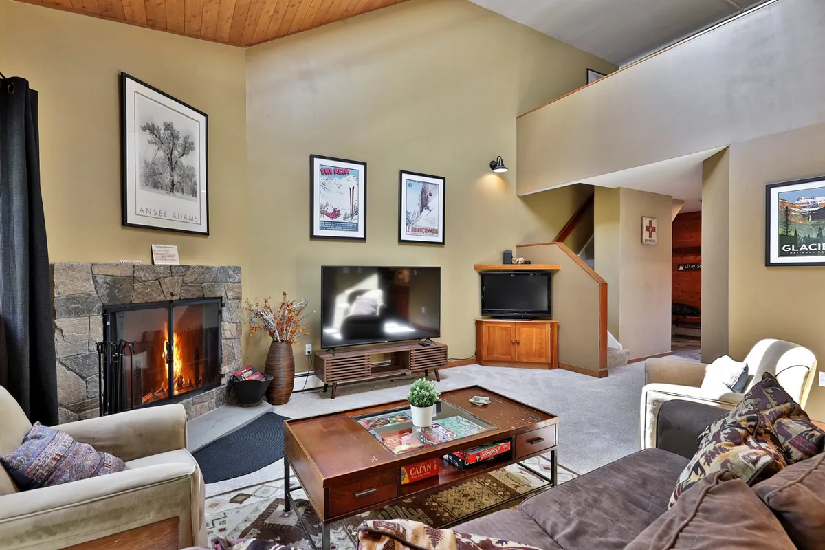A well-appointed living area with a fireplace, coffee table set up for games or snacks, comfortable seating, a smart TV, and eclectic artwork. The layout promotes both relaxation and entertainment, making it ideal for après-ski activities like movie nights or gathering with friends.