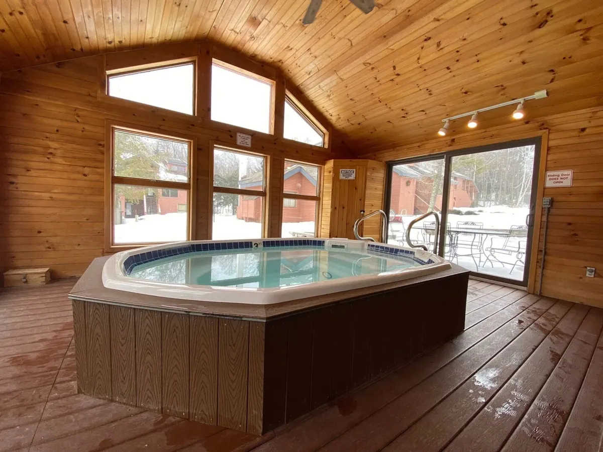 A spacious indoor hot tub sits by large windows, inviting guests to relax while enjoying views of the snowy outdoors. The wooden ceiling and warm lighting create a welcoming, resort-like atmosphere perfect for après-ski relaxation.
