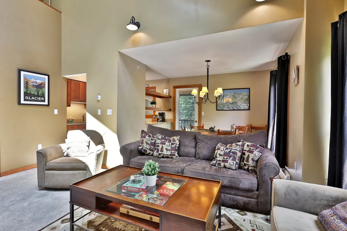 A living area with a sofa featuring patterned cushions, a wooden coffee table, and a dining area visible in the background. The scene is cozy and inviting, ideal for relaxing or accommodating guests on the sleeper sofa.