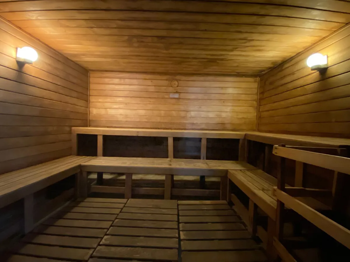 A serene sauna with wooden benches and softly glowing dim lighting, enveloped in rich wood paneling. The intimate atmosphere invites guests to relax and enjoy soothing steam sessions alone or with friends.