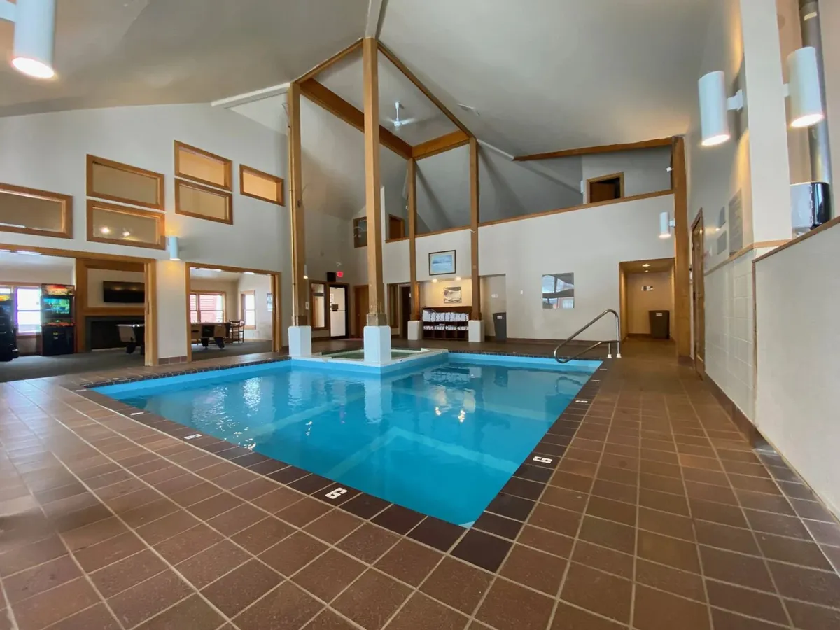 A bright, serene indoor swimming pool space with exposed wooden ceiling beams and expansive windows letting in natural light. The tranquil water and open layout invite relaxation and moments of rejuvenation after a day of adventure.