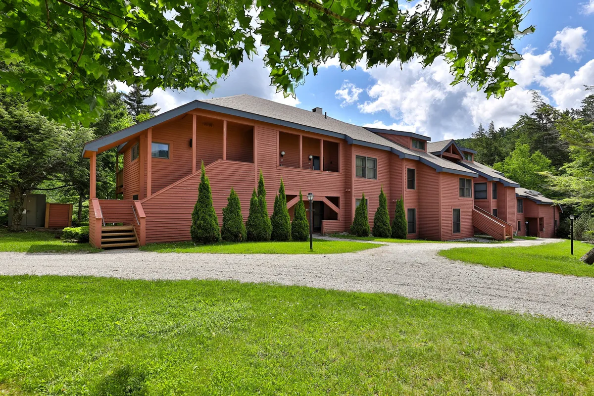 This image highlights the vibrant red exterior of the property, surrounded by neatly trimmed shrubs and a well-maintained gravel pathway. The scene suggests a welcoming environment perfect for outdoor family gatherings and easy access to nearby activities.